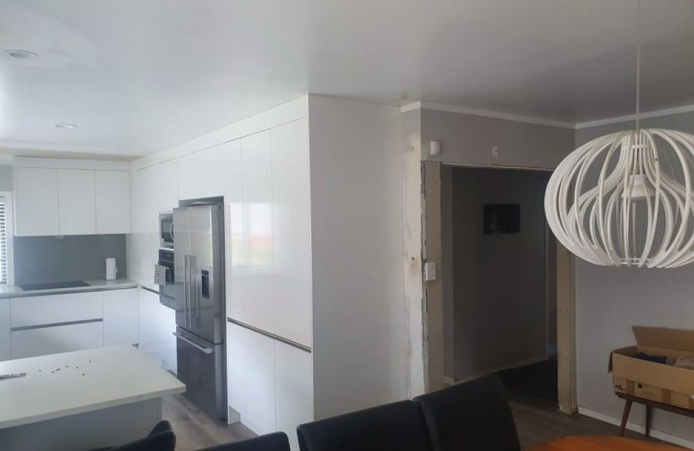 Bright modern kitchen and dining area with white cabinets, black stools, and a large pendant light