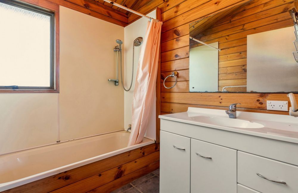 Modern bathroom with wood-paneled walls, bathtub, shower, and white vanity sink