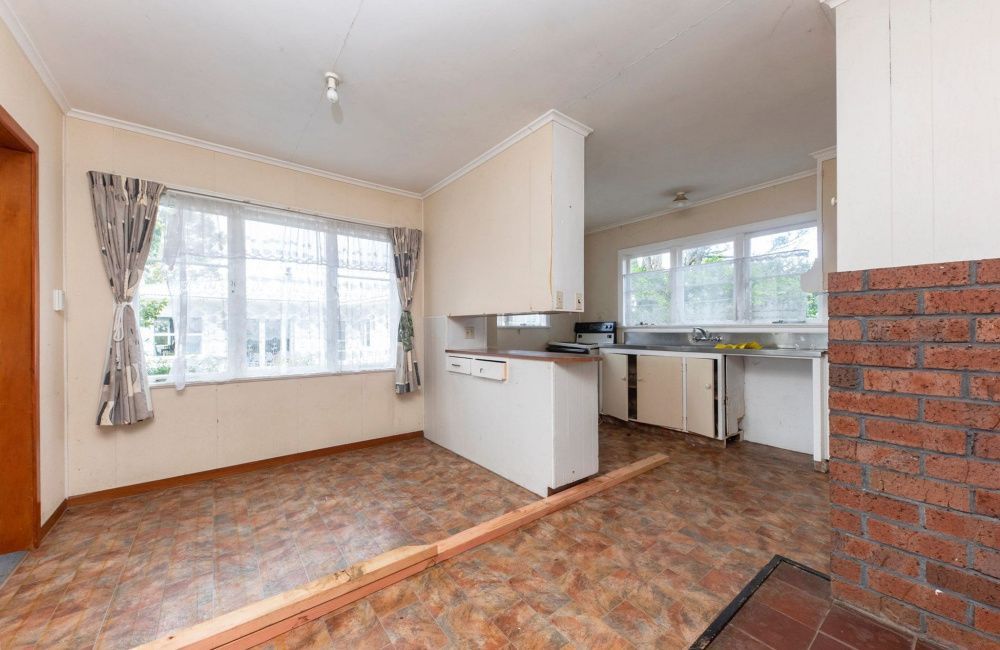 Empty beige kitchen with large window, tiled floor, and white cabinets in a bright room.