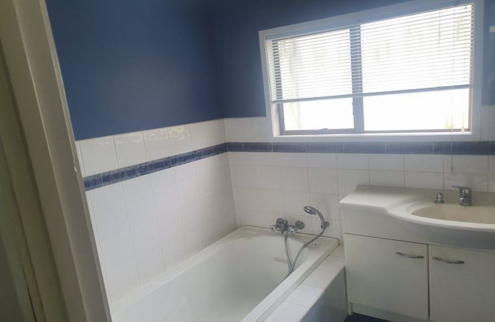 Small bathroom with blue walls, a bathtub, white sink cabinet, and window blinds.