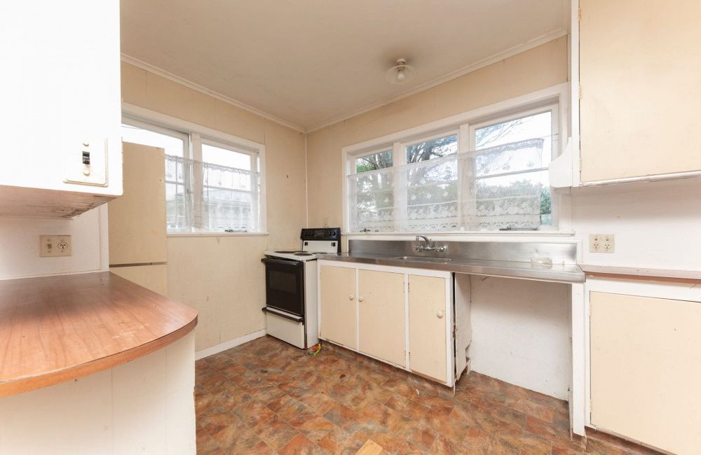 Empty beige kitchen with white cabinets, wood countertops, large windows, and a stove by the sink.