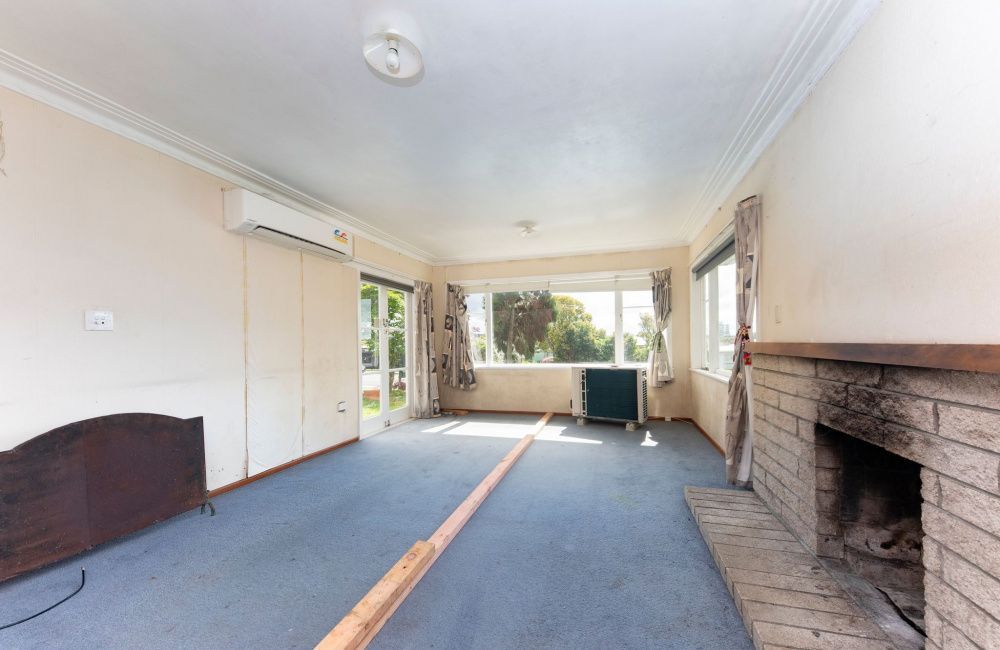 Empty living room with blue carpet, brick fireplace, and large front windows