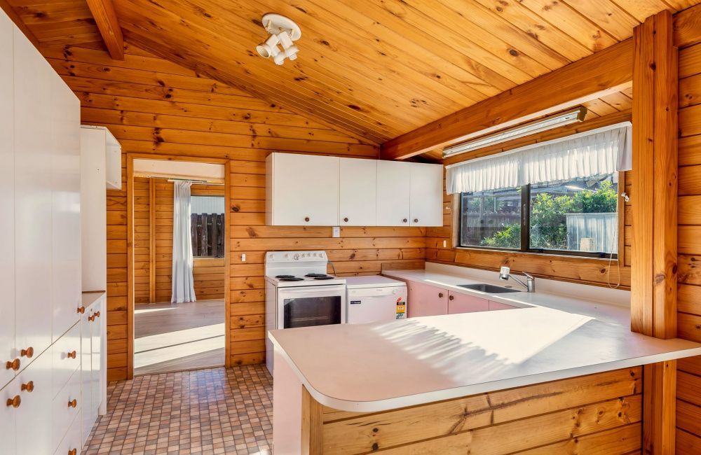 Wood-paneled kitchen with white cabinets, stove, sink, and large window overlooking greenery