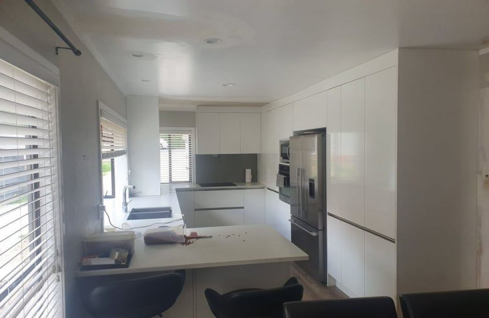 Bright modern kitchen with white cabinets, island, and stainless steel refrigerator; daylight from windows.