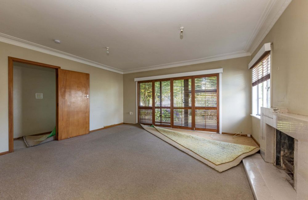 Empty living room with beige carpet, fireplace, and large windows with blinds