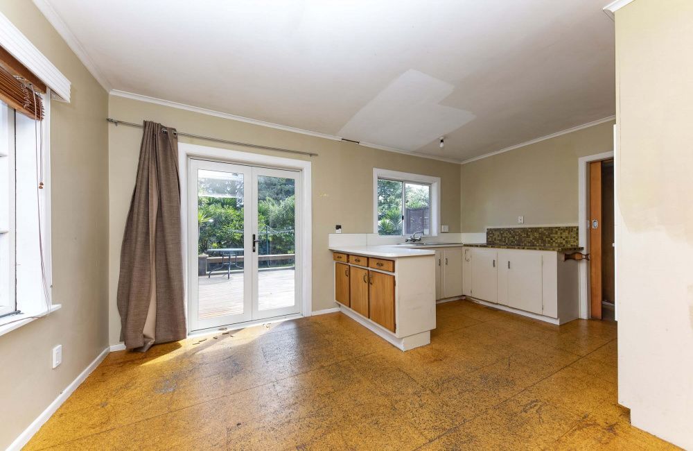 Empty kitchen with cork floor, white cabinets, and glass doors opening to a patio.