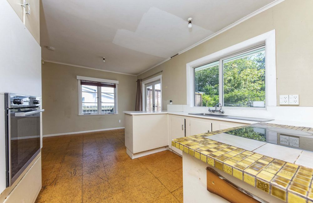 Bright kitchen with tiled counters, white cabinets, hardwood floor, and large windows overlooking greenery