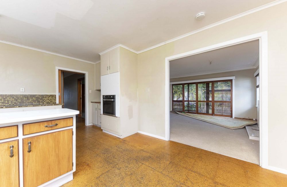 Empty kitchen opening to a bright living room with large windows and cork floor