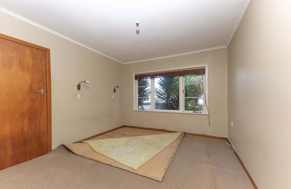Empty beige room with a window, wooden door, and a rolled-up carpet on the floor