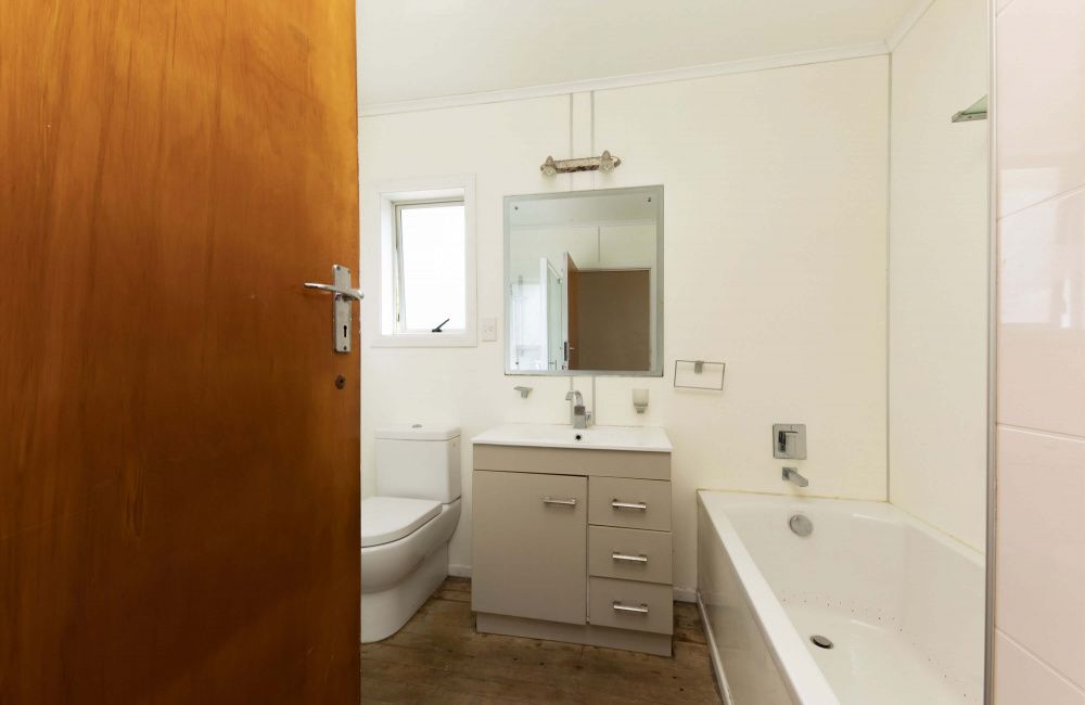 Small bathroom with toilet, vanity sink, mirror, and bathtub, seen through a partly open wooden door