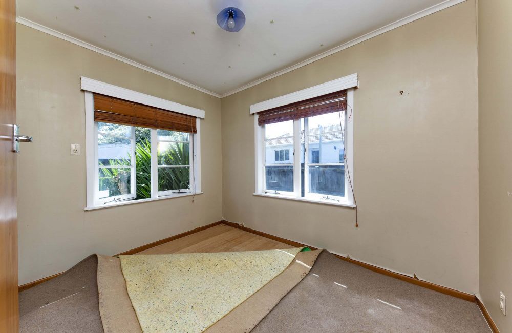 Empty beige bedroom with two windows, a bare light fixture, and a stained carpet patch on the floor