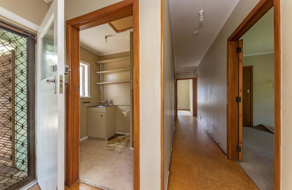 Narrow hallway with wood trim, showing a small laundry room and a bedroom or office doorway