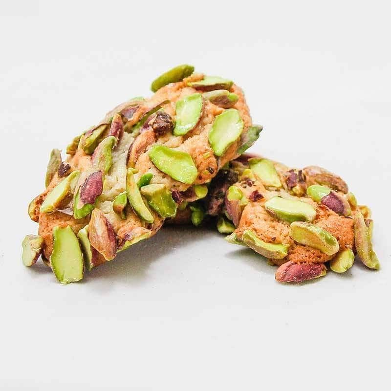 Due biscotti con pistacchi sopra sono impilati uno sopra l'altro su una superficie bianca.