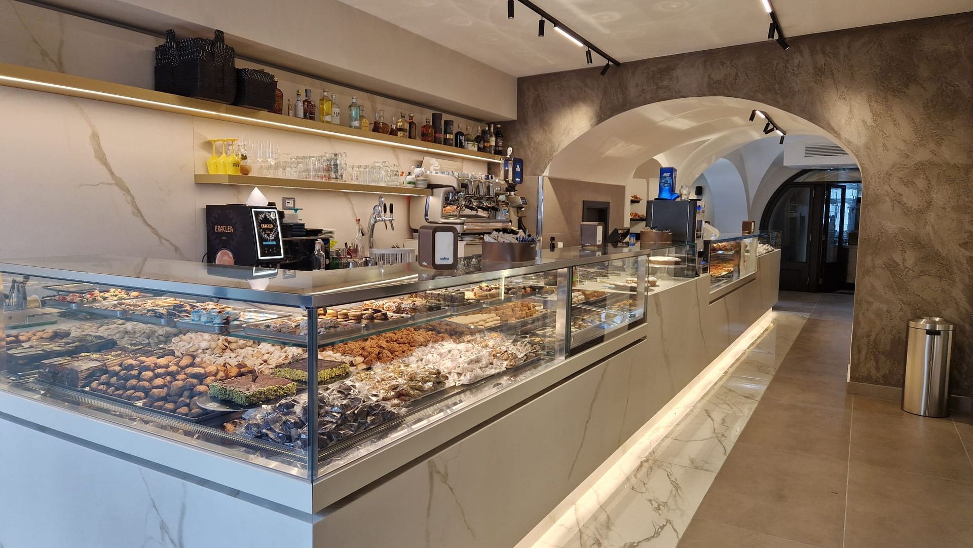 Un panificio con un lungo bancone pieno di cibo.