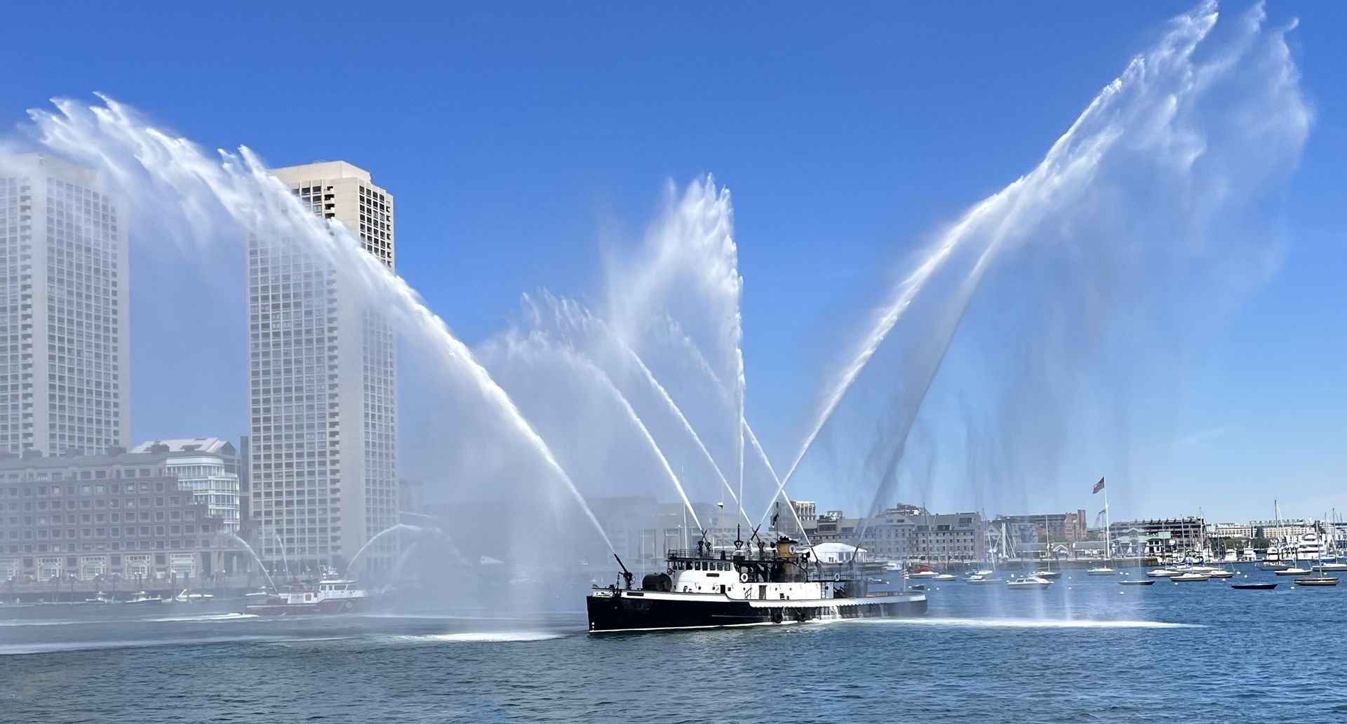 Black and white tugboat on water, spraying water from hoses. Russian flag on side. Black and white tugboat on water, spraying water from hoses. Russian flag on side.