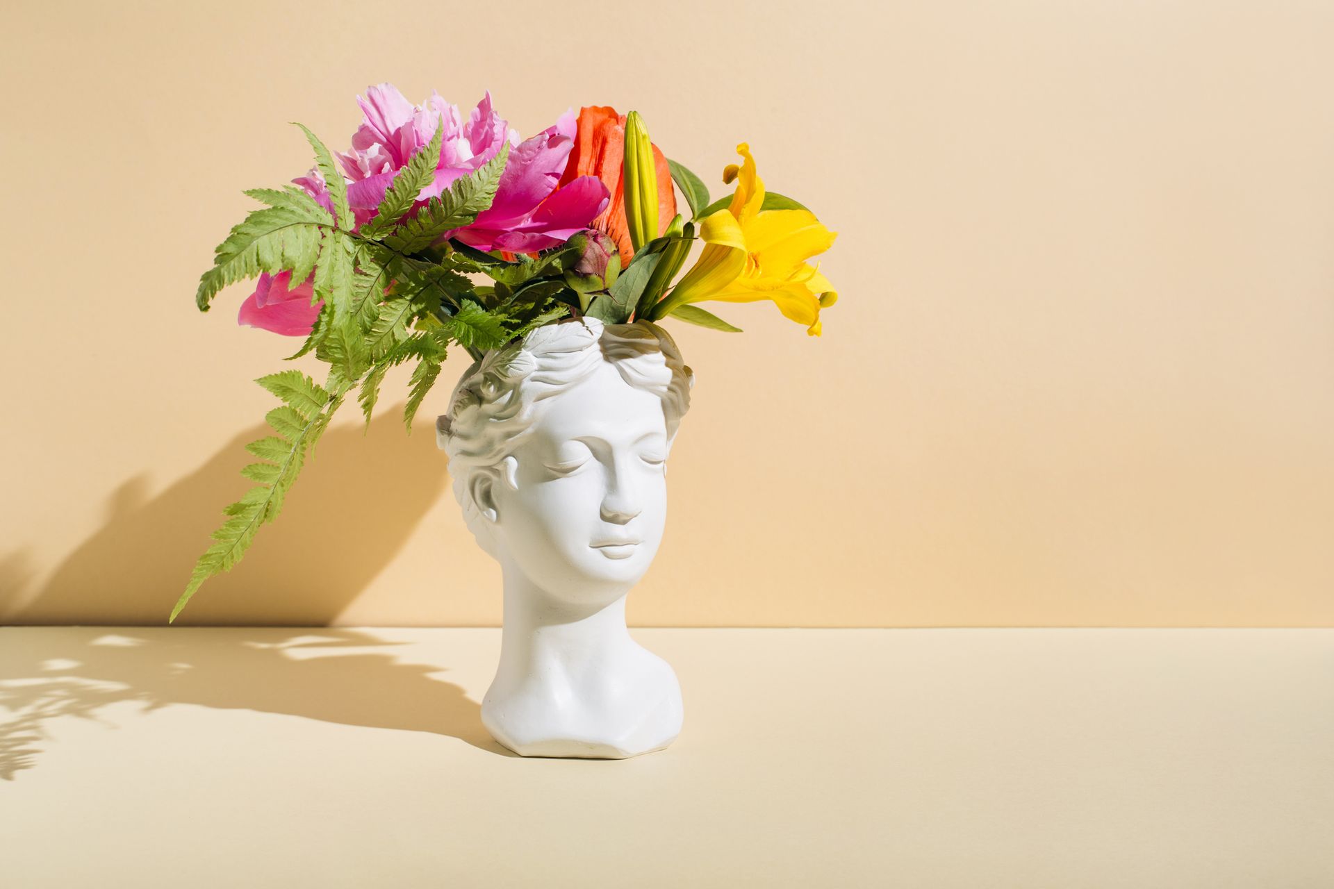 A vase in the shape of a woman 's head filled with flowers.