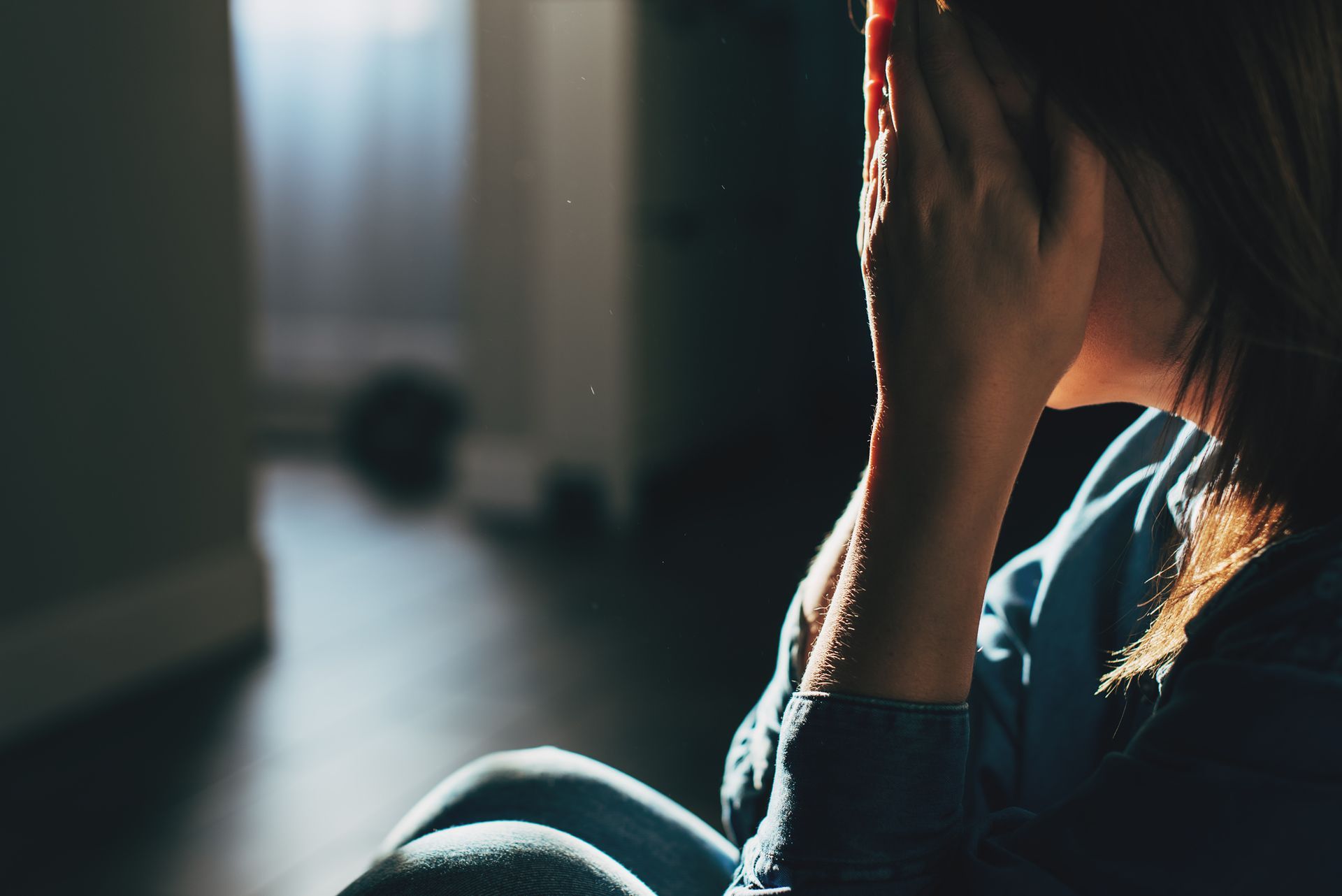 Una donna è seduta in una stanza buia con la testa tra le mani.