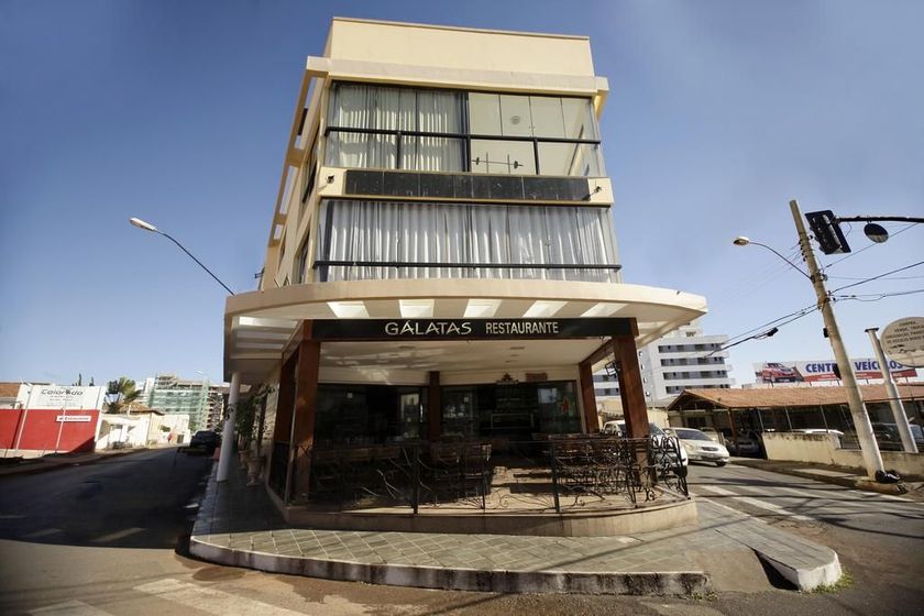 Prédio moderno em tom bege com grandes janelas e uma entrada térrea sombreada sob um céu claro.