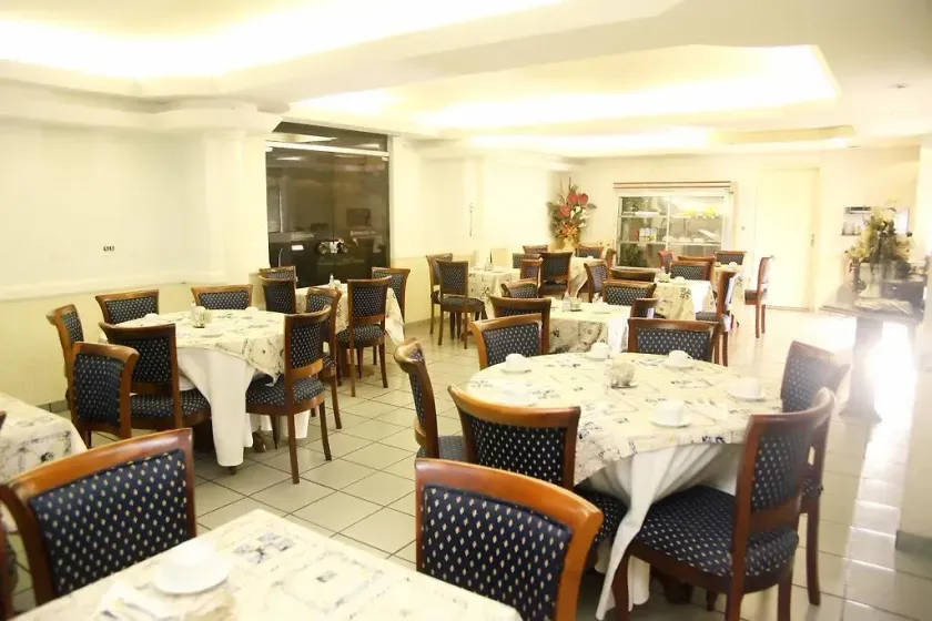 Sala de jantar de restaurante iluminada com toalhas de mesa brancas e cadeiras de madeira, mesas vazias preparadas para o serviço.