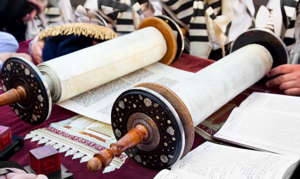 Two Torah scrolls with wooden handles, on a table with an open book, used in Jewish religious ceremonies.
