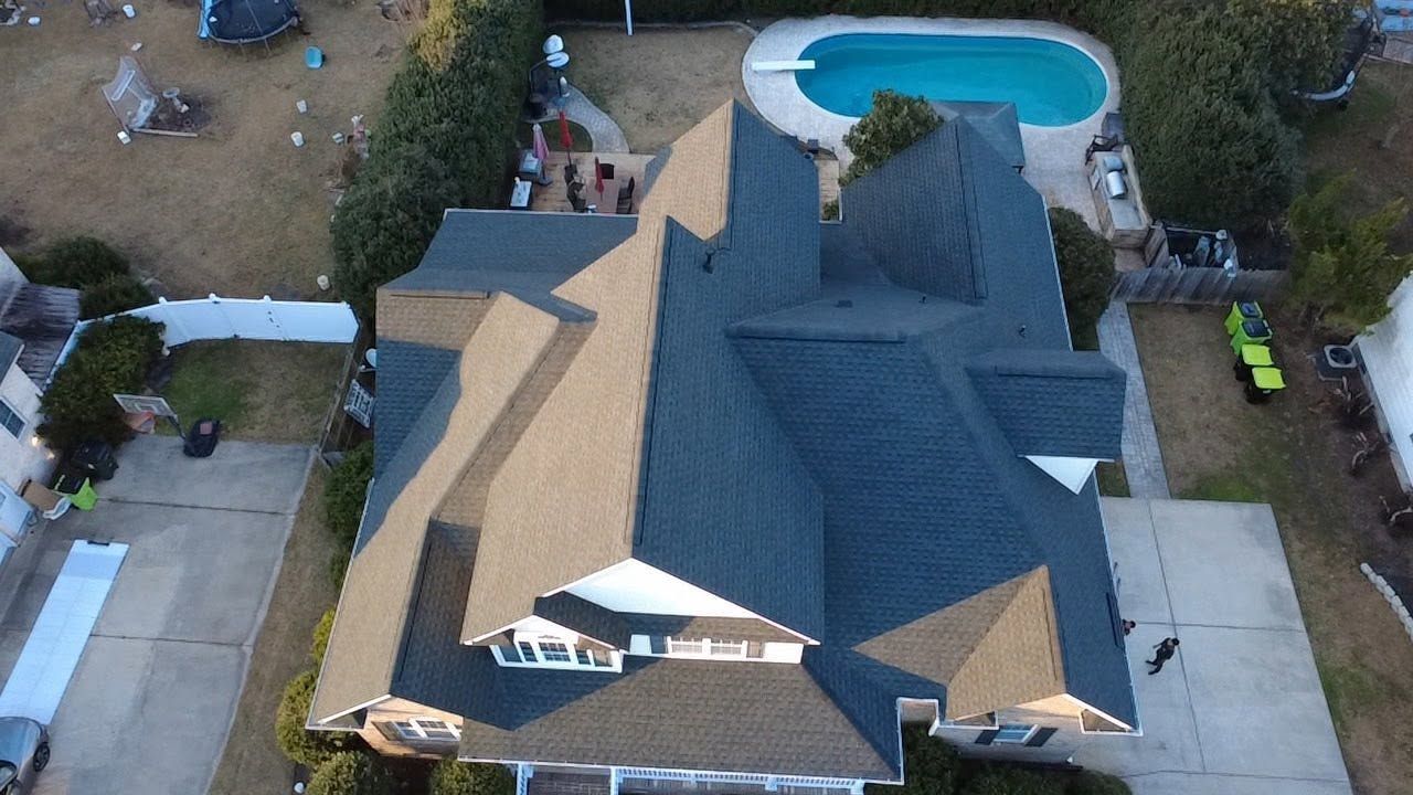 Aerial view of a house with a gray roof and backyard pool, surrounded by trees and driveways