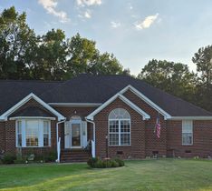 Brick ranch-style house with white trim, front lawn, and trees in the background at sunset