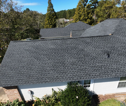 Gray shingled roof on a white house, seen from above with trees in the background
