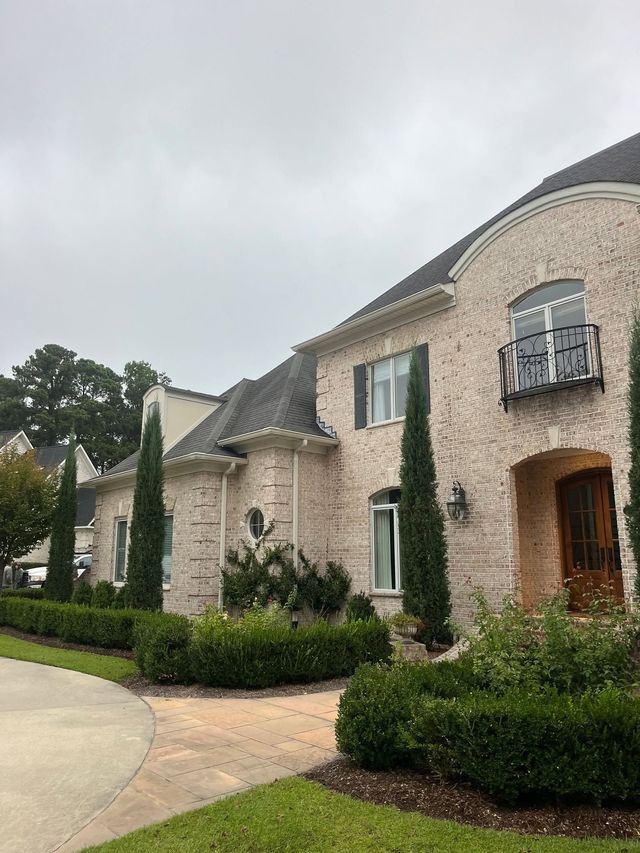 Stone townhouse with arched doorway, balcony, and manicured shrubs along a curved driveway
