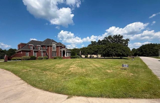 Brick house with white columns, large grassy lawn, and blue sky with scattered clouds