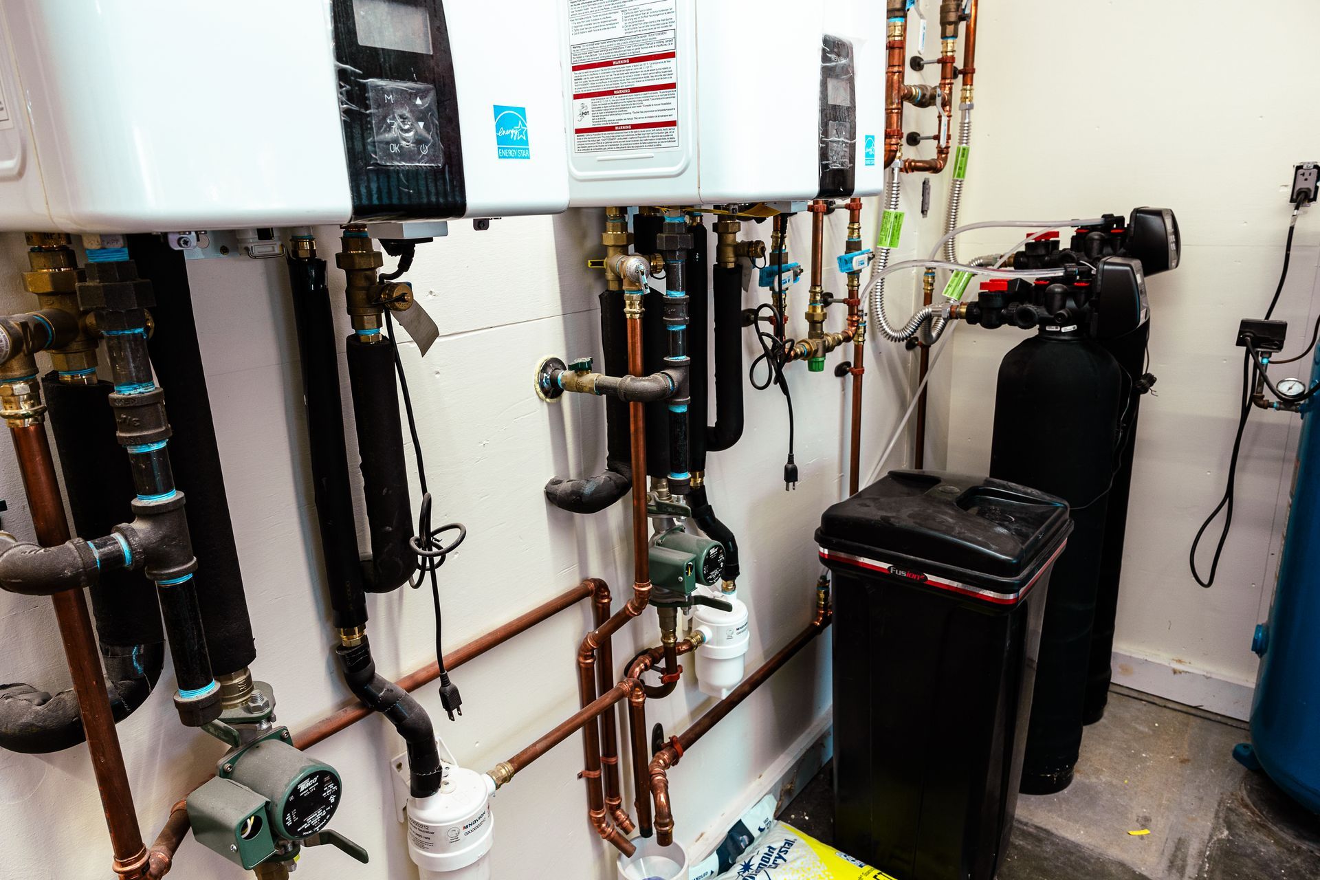 A room with a lot of pipes and a boiler on the wall.