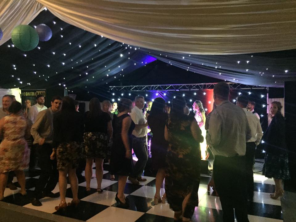 A group of people are dancing on a checkered dance floor in a tent.