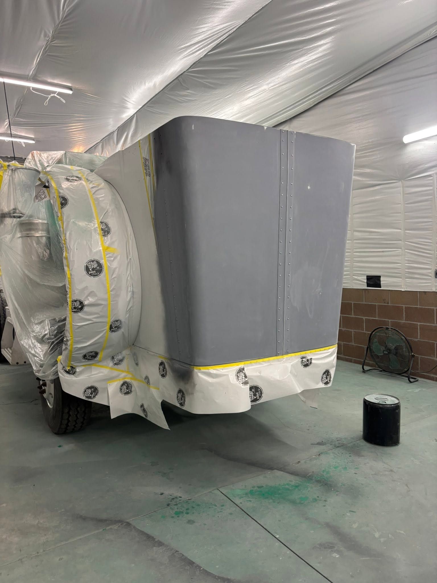 Covered vehicle under repair in a garage, wrapped in plastic with gray primer panels exposed.