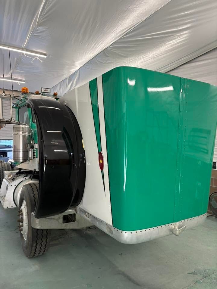 Large green and white utility trailer with black wheel on a concrete floor inside a covered structure
