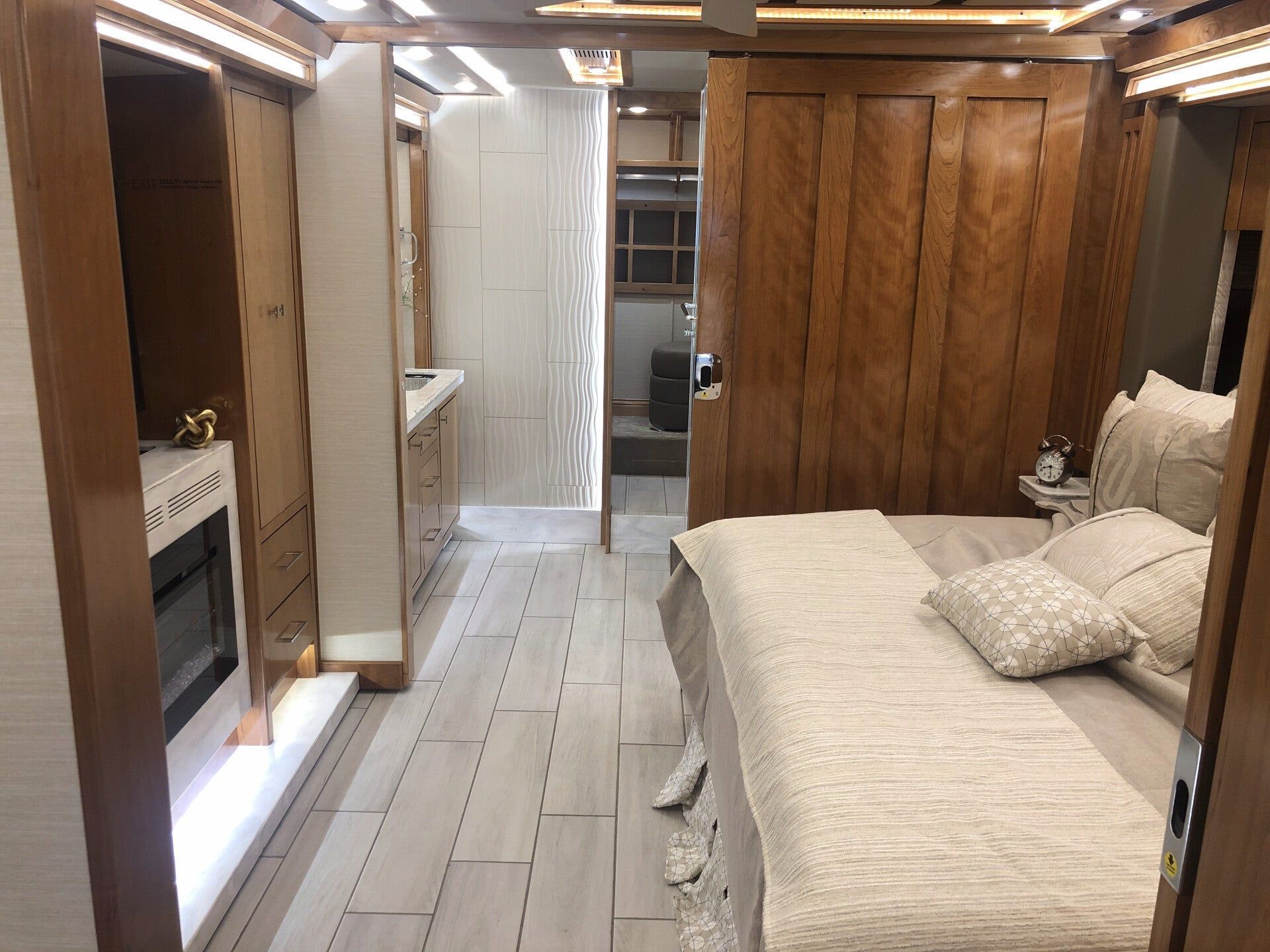 Narrow bedroom with bed, wood-paneled wall, and a small adjoining bathroom in the background