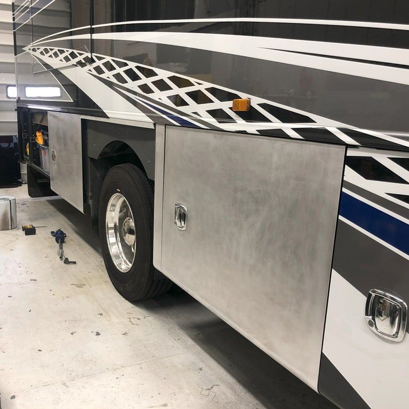 Large bus or RV with silver side panel and black-and-white stripe pattern in a garage or workshop.