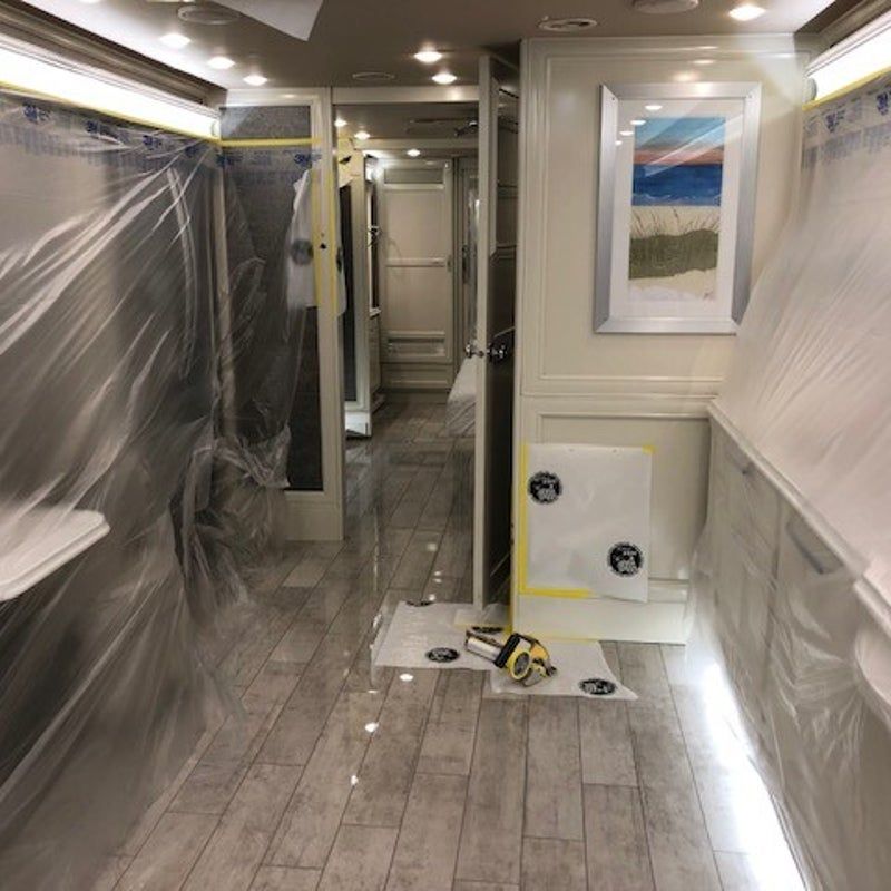 Hallway under renovation with plastic-covered walls, gray tile floor, and a framed beach print on the wall