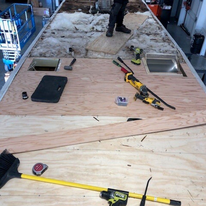 Roof repair work on a trailer roof with tools, vents, and plywood panels laid out