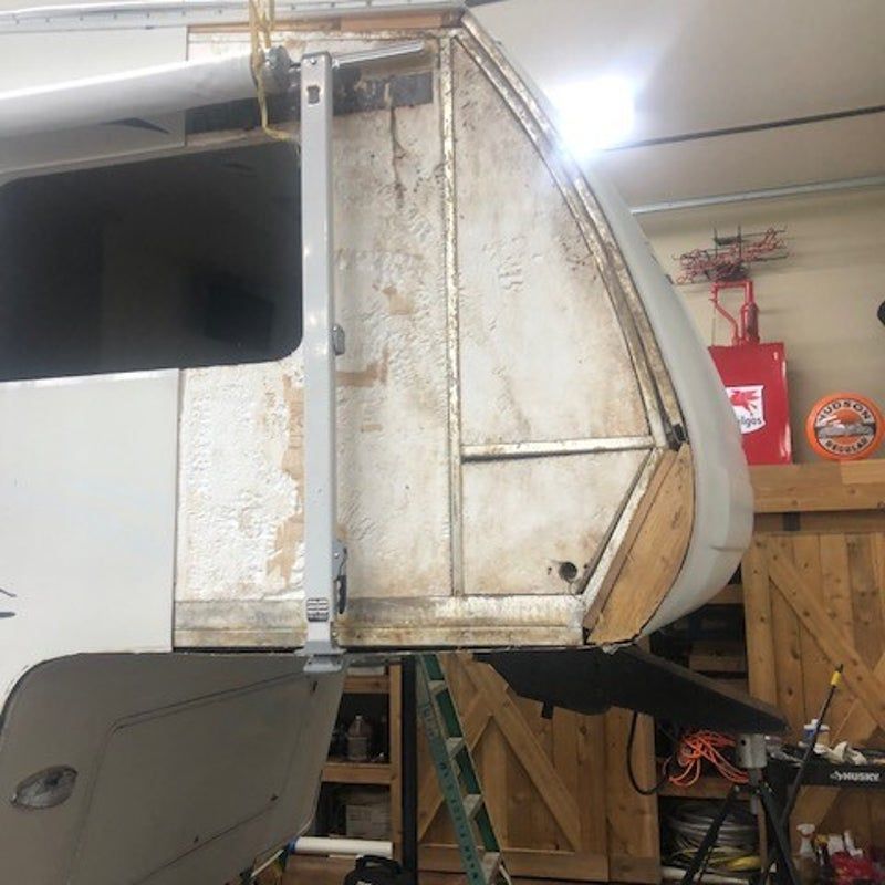 Old white camper shell in a wooden garage, showing a worn, rounded front section.