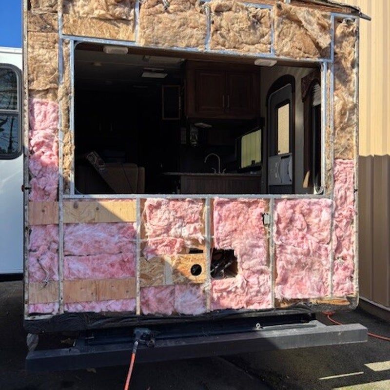 Exposed pink insulation on the exterior of a RV, with a large opening revealing the interior kitchen.