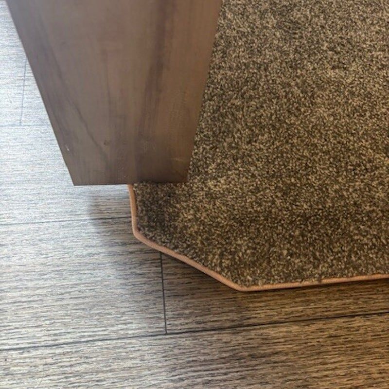 Brown cabinet beside a speckled carpet mat on a wood floor