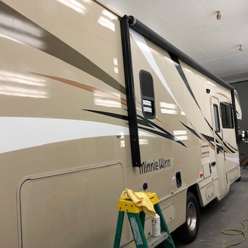 Beige and white RV in a garage, with a green step ladder and hose nearby.