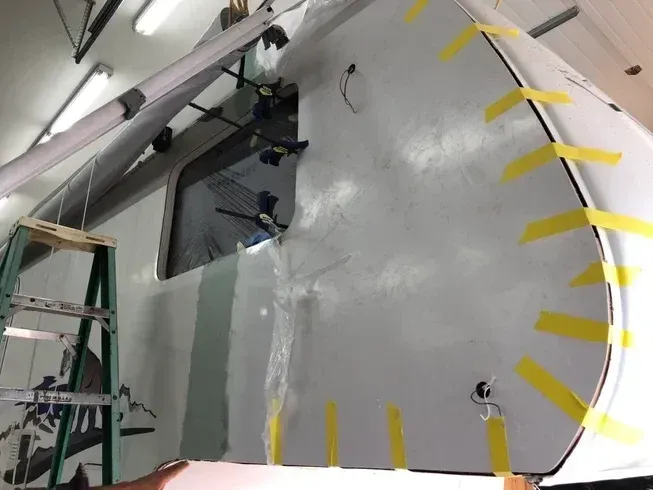 Worker applying tape to a gray wall in an industrial room, with a ladder and tools nearby