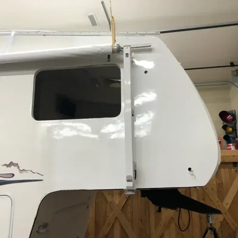 White camper shell with window and side hatch mounted in a garage, seen close-up from the side