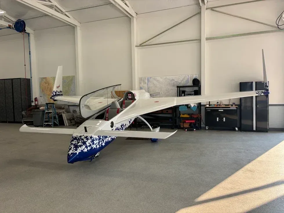 Small white-and-blue single-engine plane parked inside a hangar workshop with tools and storage cabinets.