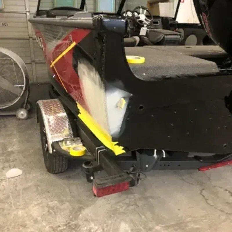 Damaged black car rear quarter panel with red and yellow paint scrape in a garage