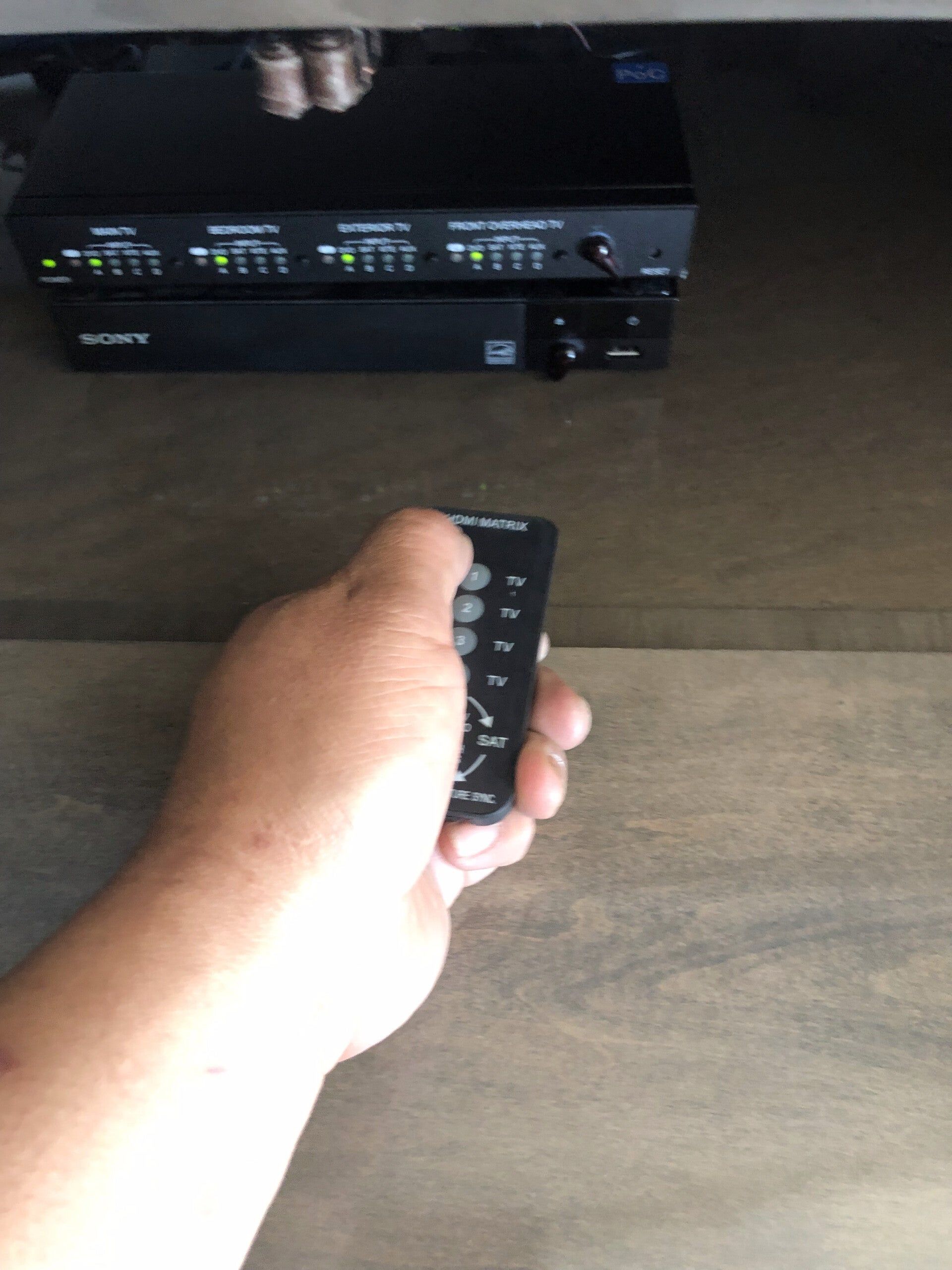 Hand holding a remote aimed at a black Sony device on a shelf