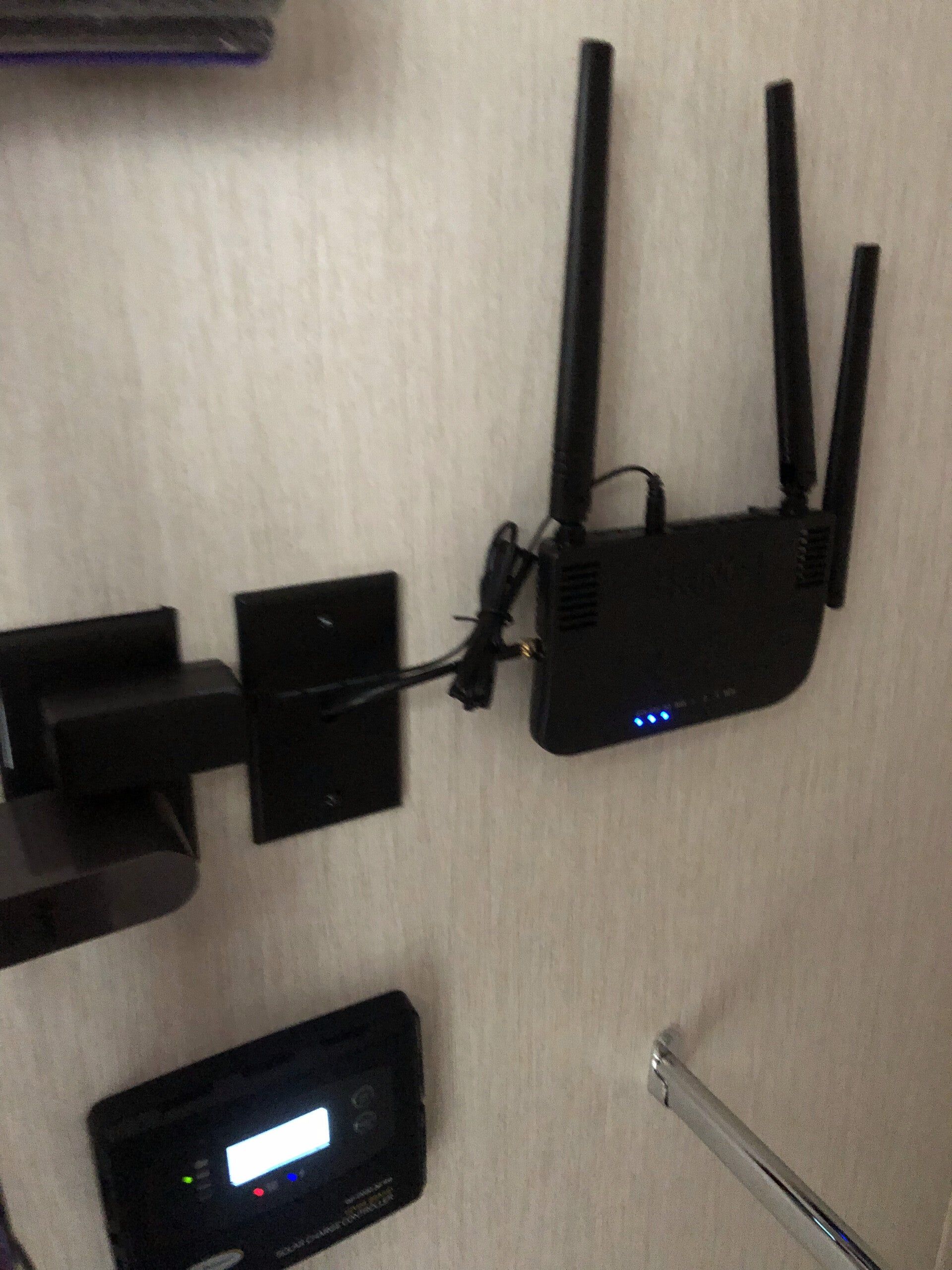 Wall-mounted Wi‑Fi router with antennas and blue status lights, above a small screen on the wall.