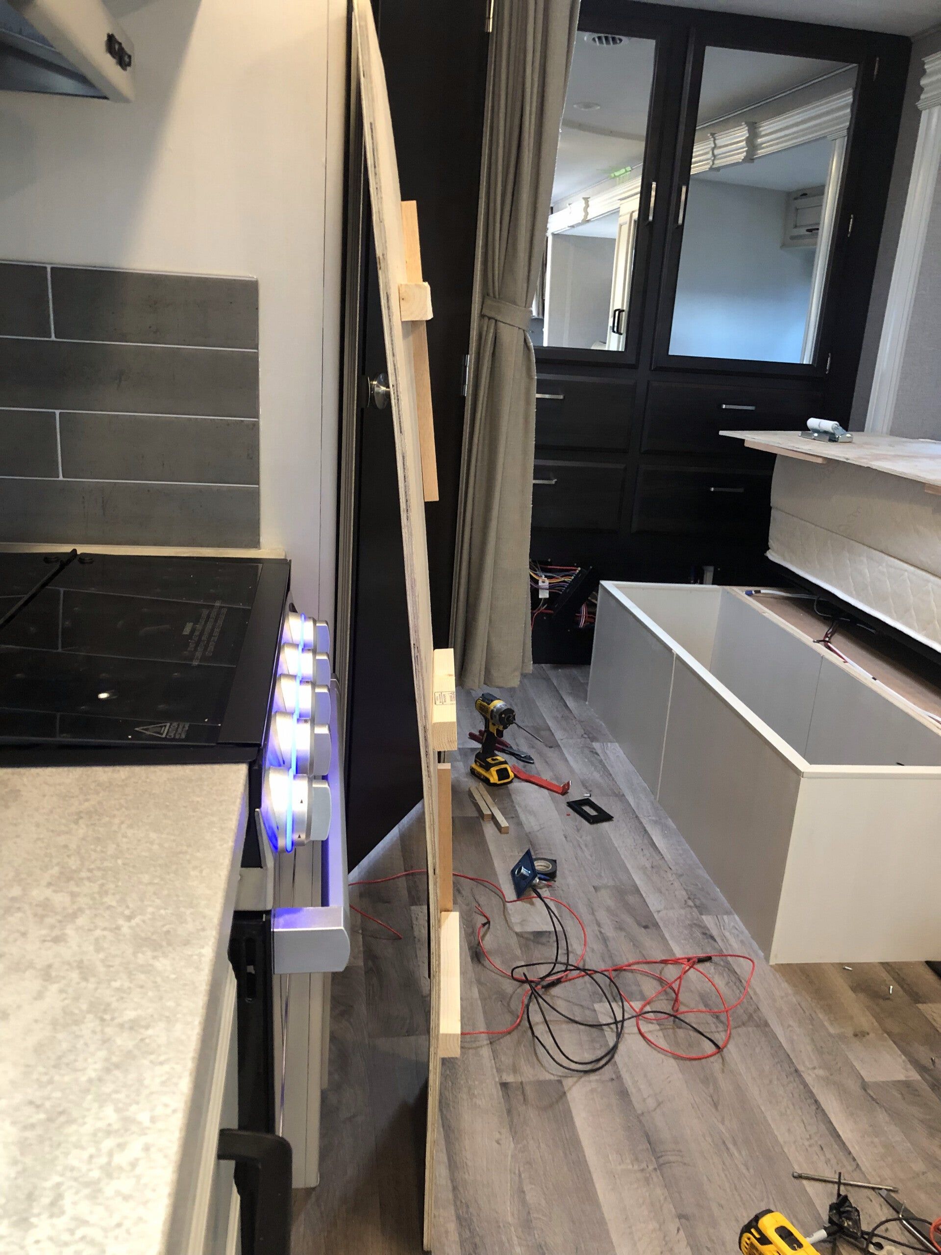 Narrow kitchen under renovation with cabinets, tools, wires, and a white island base on a gray floor
