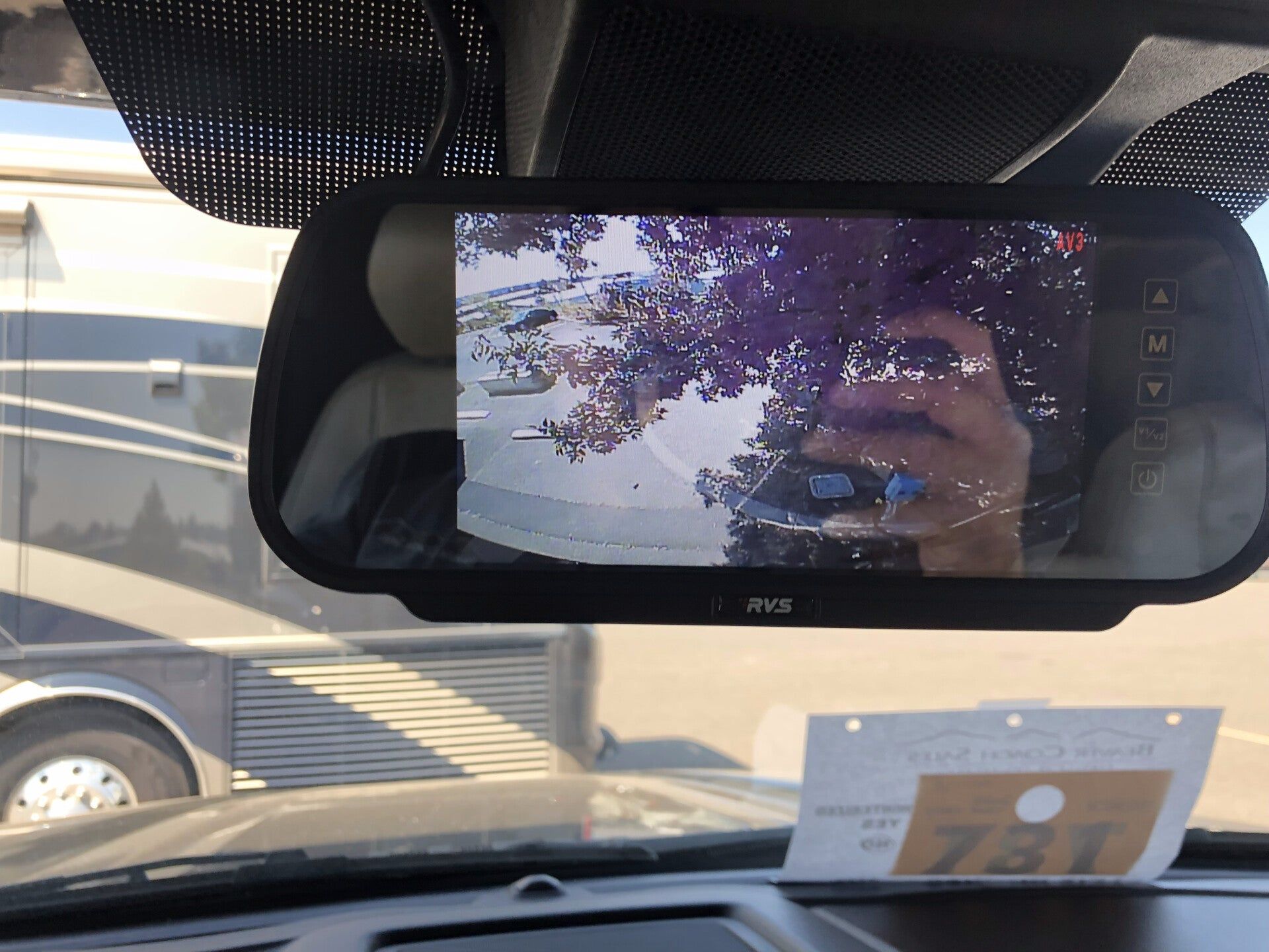 Car dashboard with rearview mirror reflecting a person and trees outside, plus a card on the windshield