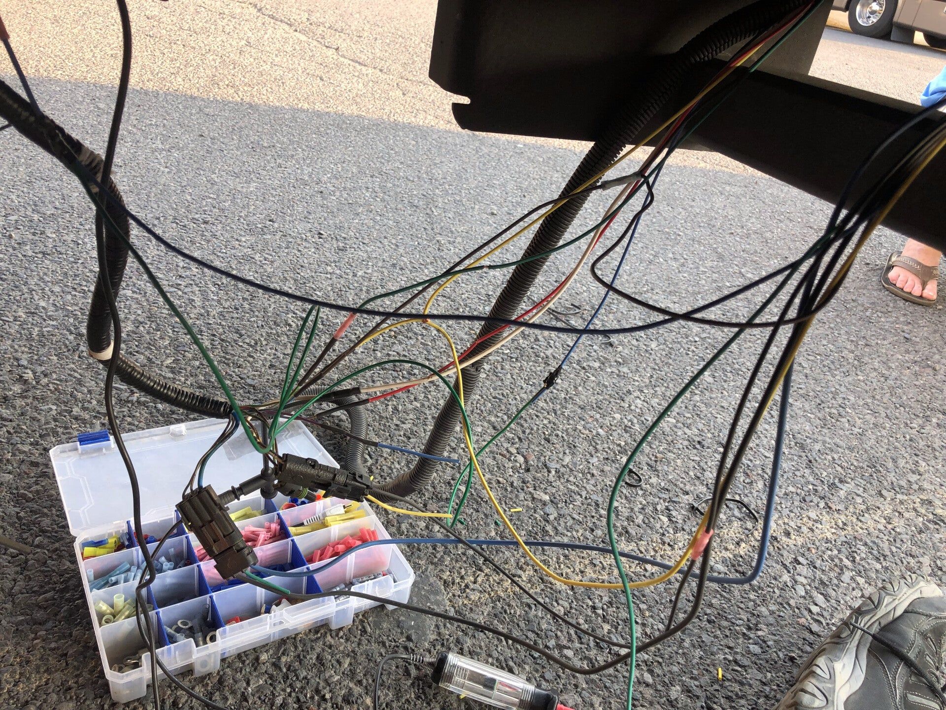 Messy bundle of wires and connectors on pavement beside a cart, with colorful cables and boxes.